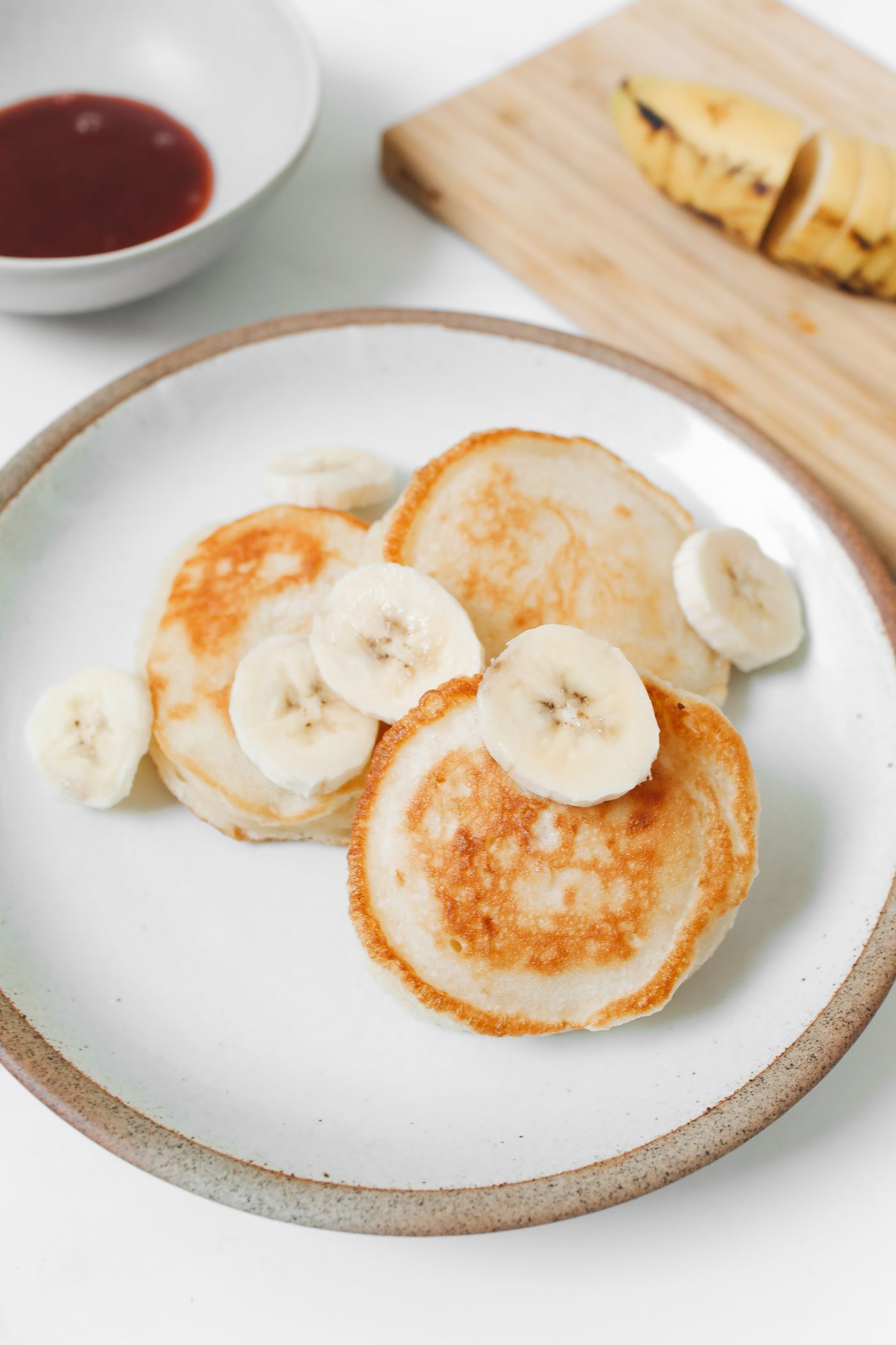 Stack of homemade pancakes topped with banana slices on a white plate