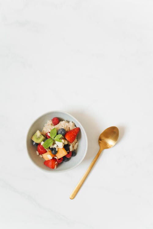 Sliced Fruits in a Bowl Near a Gold Spoon on a White Surface
