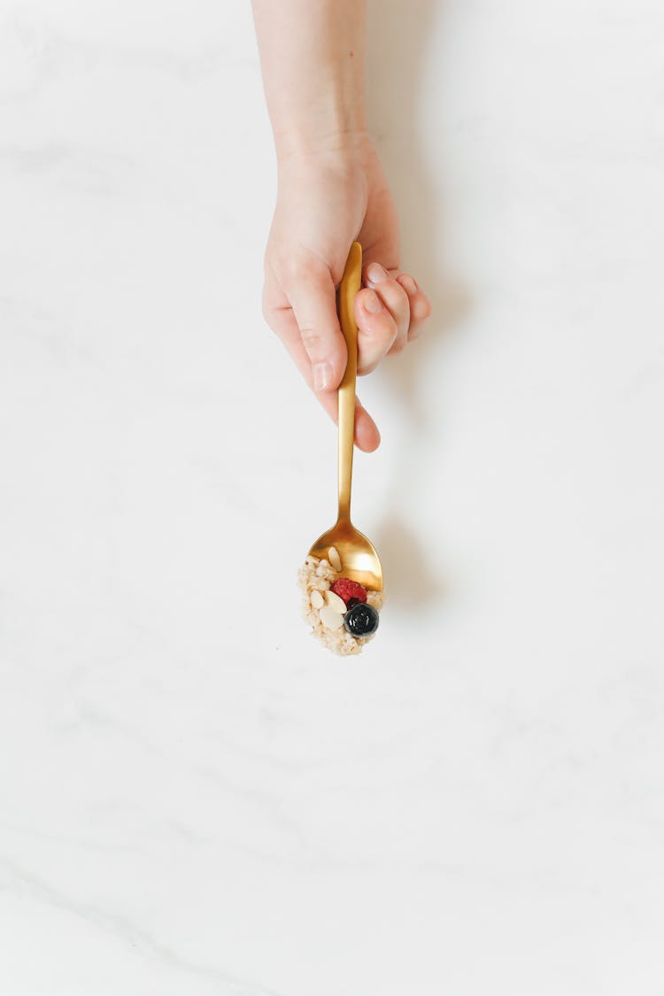 Woman Holding Nuts And Berries On A Golden Spoon 