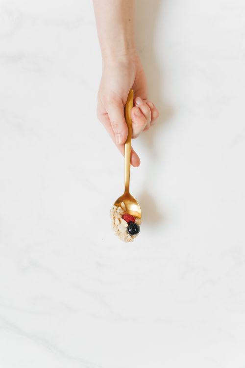 Free Hand holding a golden spoon with mixed berries and nuts, on a marble counter. Stock Photo
