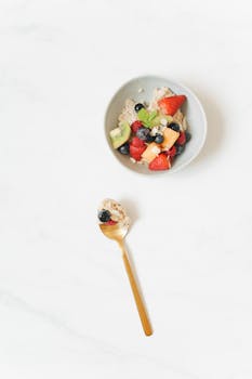 Top view of a healthy breakfast bowl with assorted fresh fruits and oats on a white surface.