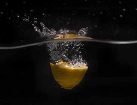 Refreshing lemon slice submerged in water with dramatic splash effect on a black background.