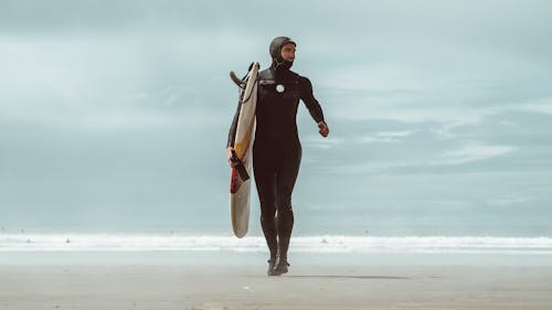 Surfer Holding a Surfboard Walking on a Beach 