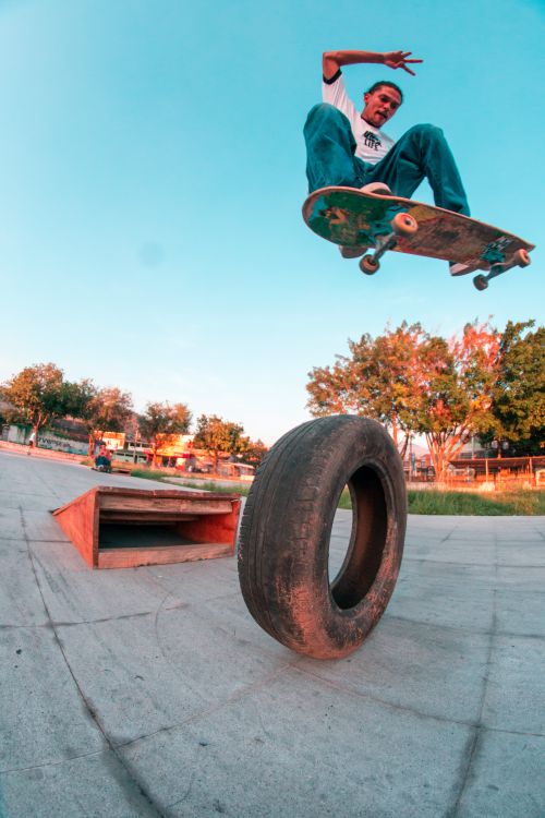 Free Low angle of risky male learning new skills with longboard and leaping high above tire Stock Photo