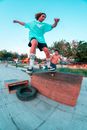 Full body of young ethnic skater doing extreme tricks on longboard while friend watching stunt and waiting