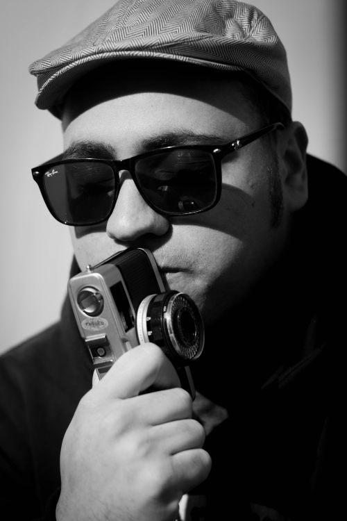 Free Black and white thoughtful male with eyes closed wearing stylish sunglasses and hat while touching lips with photo camera in contemplation Stock Photo