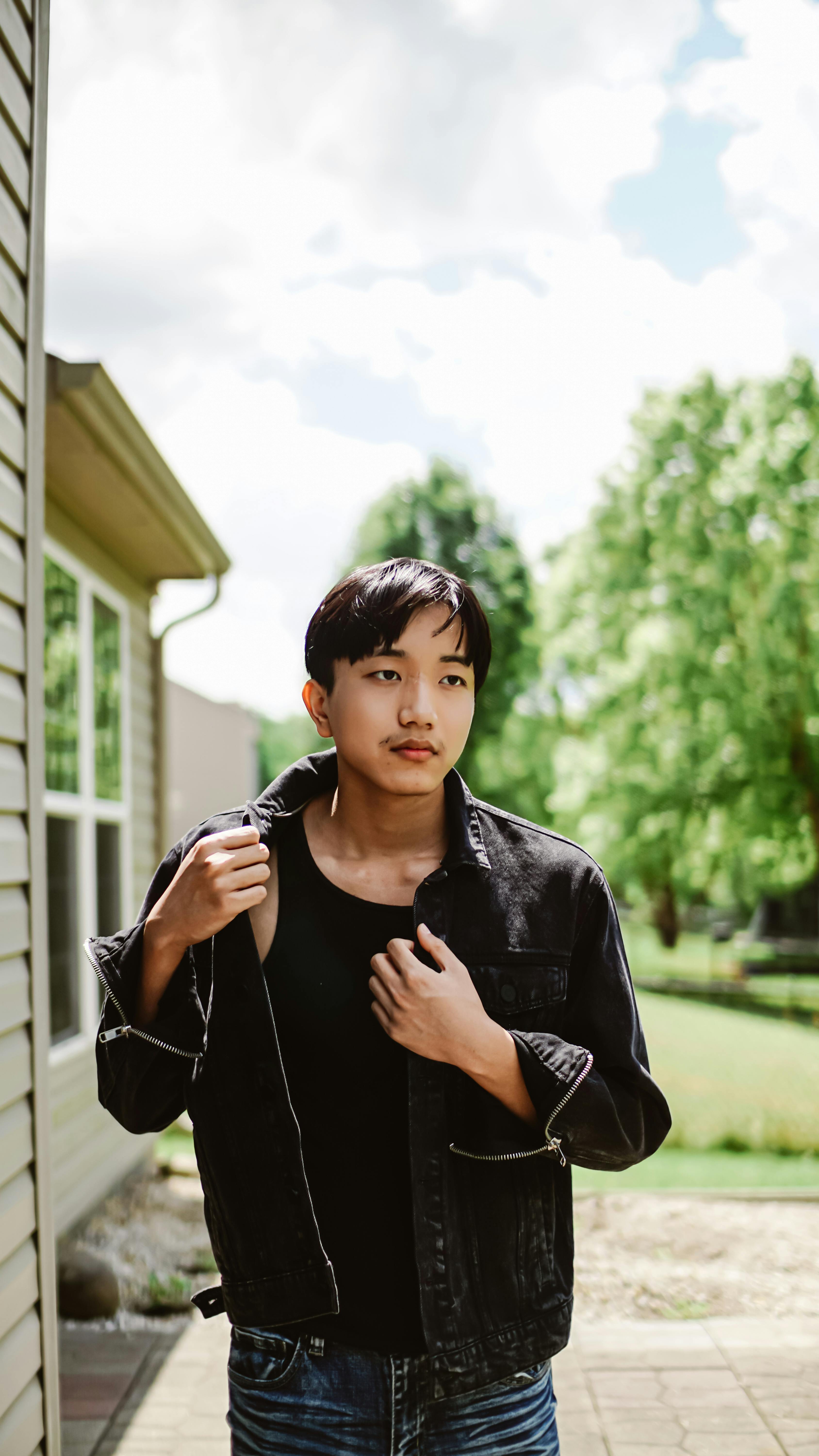 Portrait of a young man in a denim jacket standing outdoors on a sunny day.