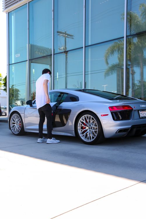 Free Full body back view of male in white t shirt and black trousers standing next to modern luxury vehicle in daylight Stock Photo