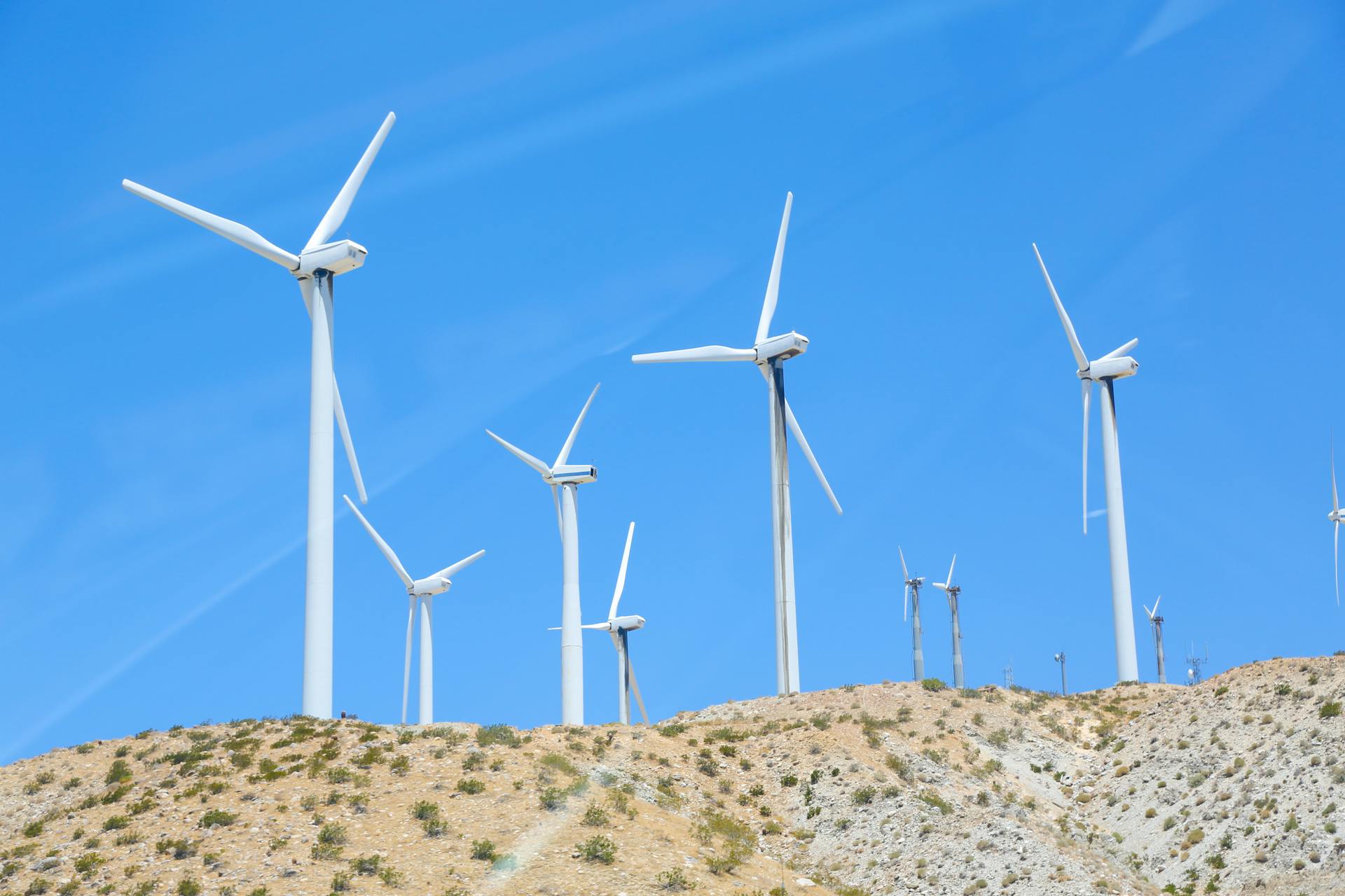 From below of tall wind energy converters with long thick steel towers and rotor blades under blue sky in sunlight