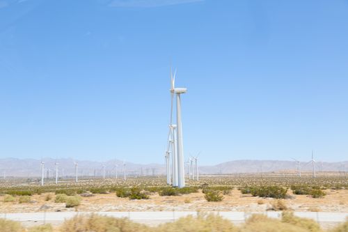 Free Tall wind generators with thick steel towers and long thin rotor blades under blue sky in meadow covered with bushes in sunlight Stock Photo