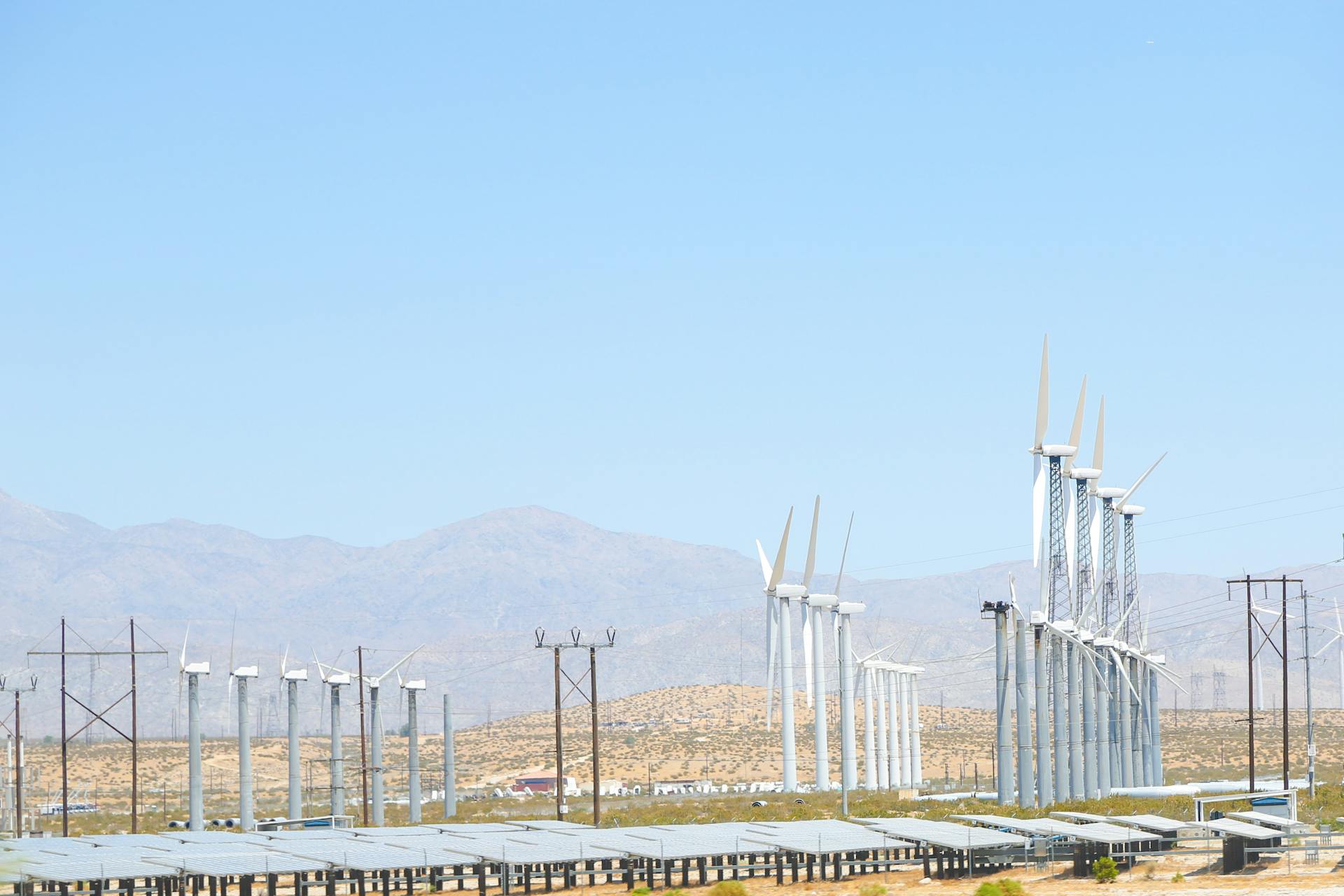 Array of wind turbines generating renewable energy under a clear blue sky in a dry desert environment.