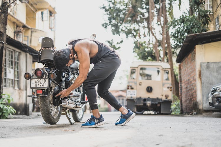 Man In Black Shirt And Pants Fixing A Parked Motorcycle