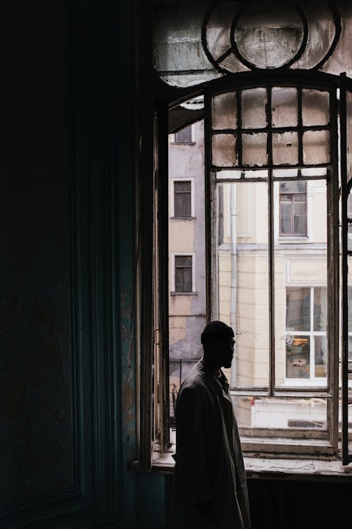Man in Black Jacket Standing in Front of Window