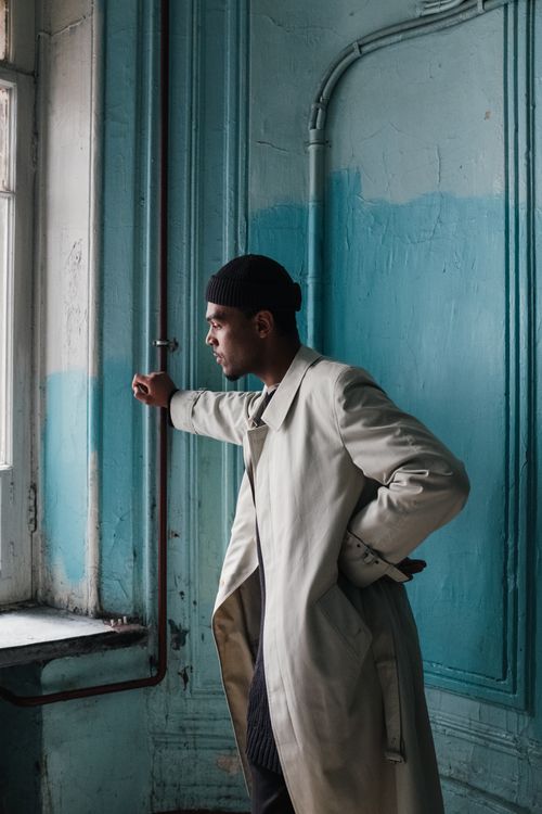 Free Man in beige coat looking out window in vintage interior with natural light and peeling walls. Stock Photo