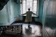 一名身穿米色外套的男子站在一栋老建筑的复古楼梯上，建筑内光线自然