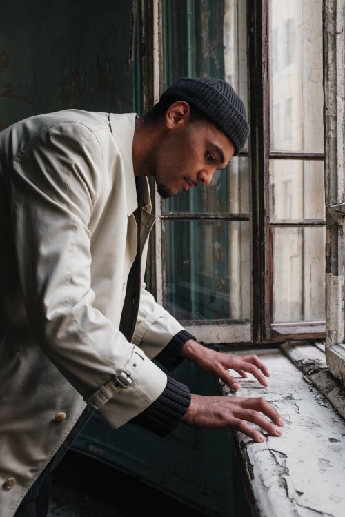 Free A man in a beige coat leaning on a windowsill with vintage decor. Stock Photo