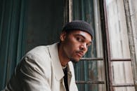 一位穿着米色外套、戴着黑色帽子的时尚男子在复古窗户旁摆姿势