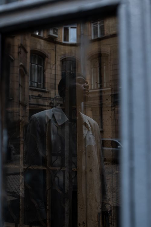 Free A man stands reflected in a window against a vintage courtyard backdrop. Stock Photo