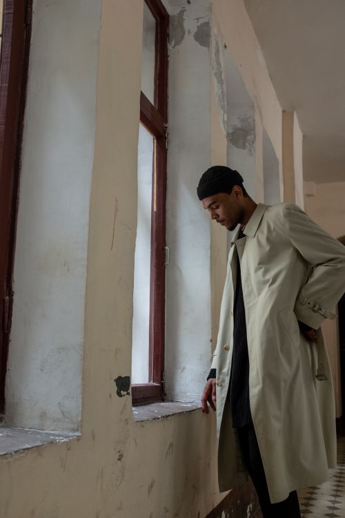 Free A man in a beige coat stands in an old hallway with peeling walls and natural light. Stock Photo