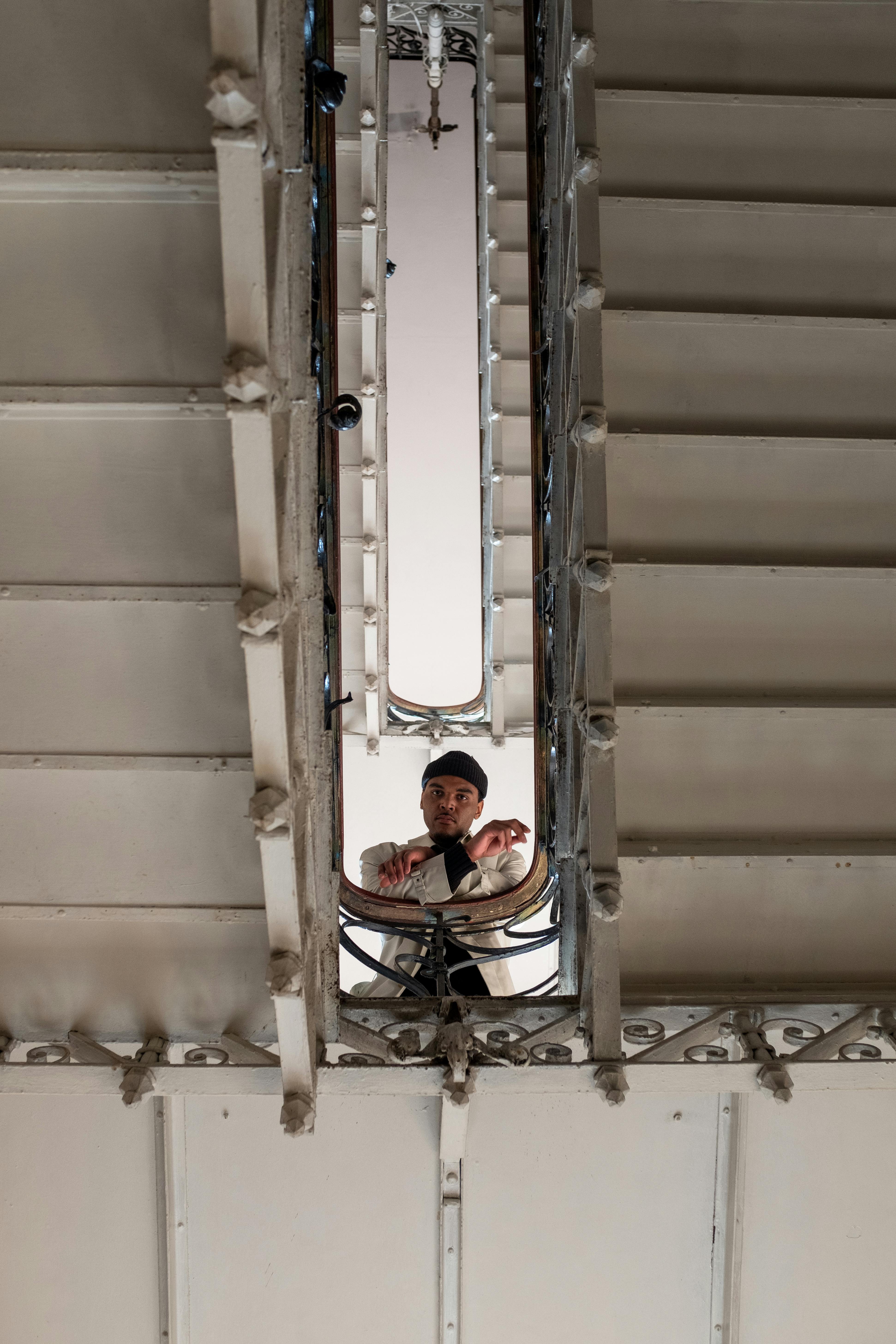 A man at the bottom of a vintage spiral staircase, seen through the opening.
