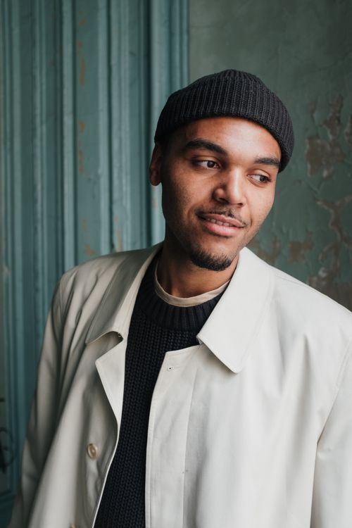 Free Portrait of a stylish man wearing a beige coat and black hat in an old building with natural light. Stock Photo