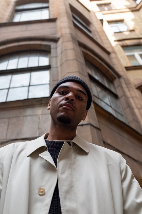 Free Portrait of a man in a beige coat and black hat in front of a classic building facade. Stock Photo