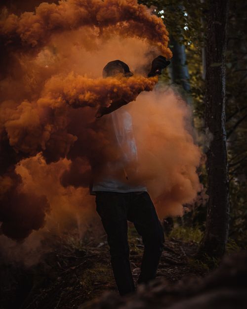 Free Person in forest with billowing orange smoke, creating a mysterious and dramatic scene. Stock Photo