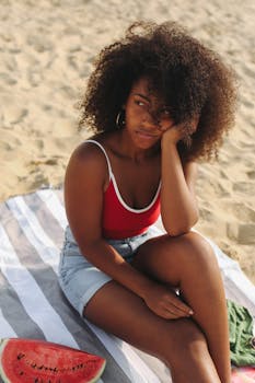 Woman enjoying leisure time at the beach sitting on a towel with a slice of watermelon.