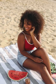 A woman sits on the beach with a slice of watermelon, enjoying a sunny summer day.