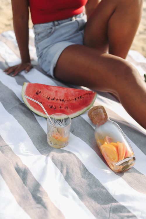 Free Relaxed summer scene with watermelon and lemonade on a beach towel, evoking leisure and refreshment. Stock Photo