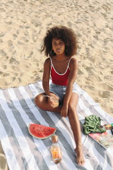 一位女士在海滩上喝着饮料、吃着西瓜，享受阳光明媚的一天