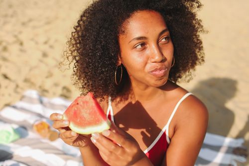 Free Smiling woman savoring a watermelon slice on a sunny beach day, radiating summer vibes. Stock Photo