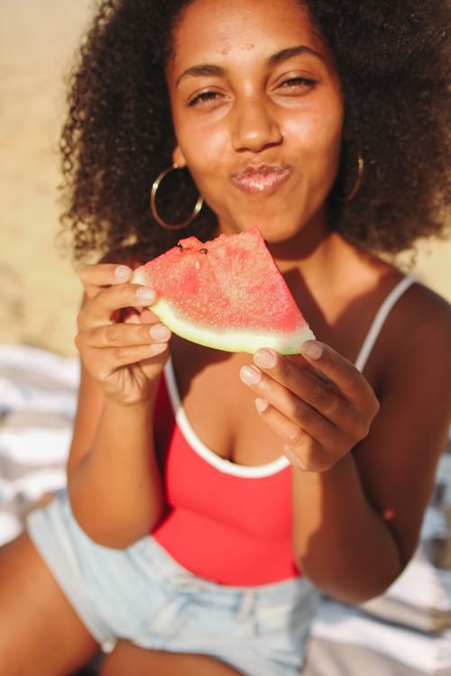 Free Happy woman enjoying a fresh slice of watermelon on a sunny summer day at the beach. Stock Photo