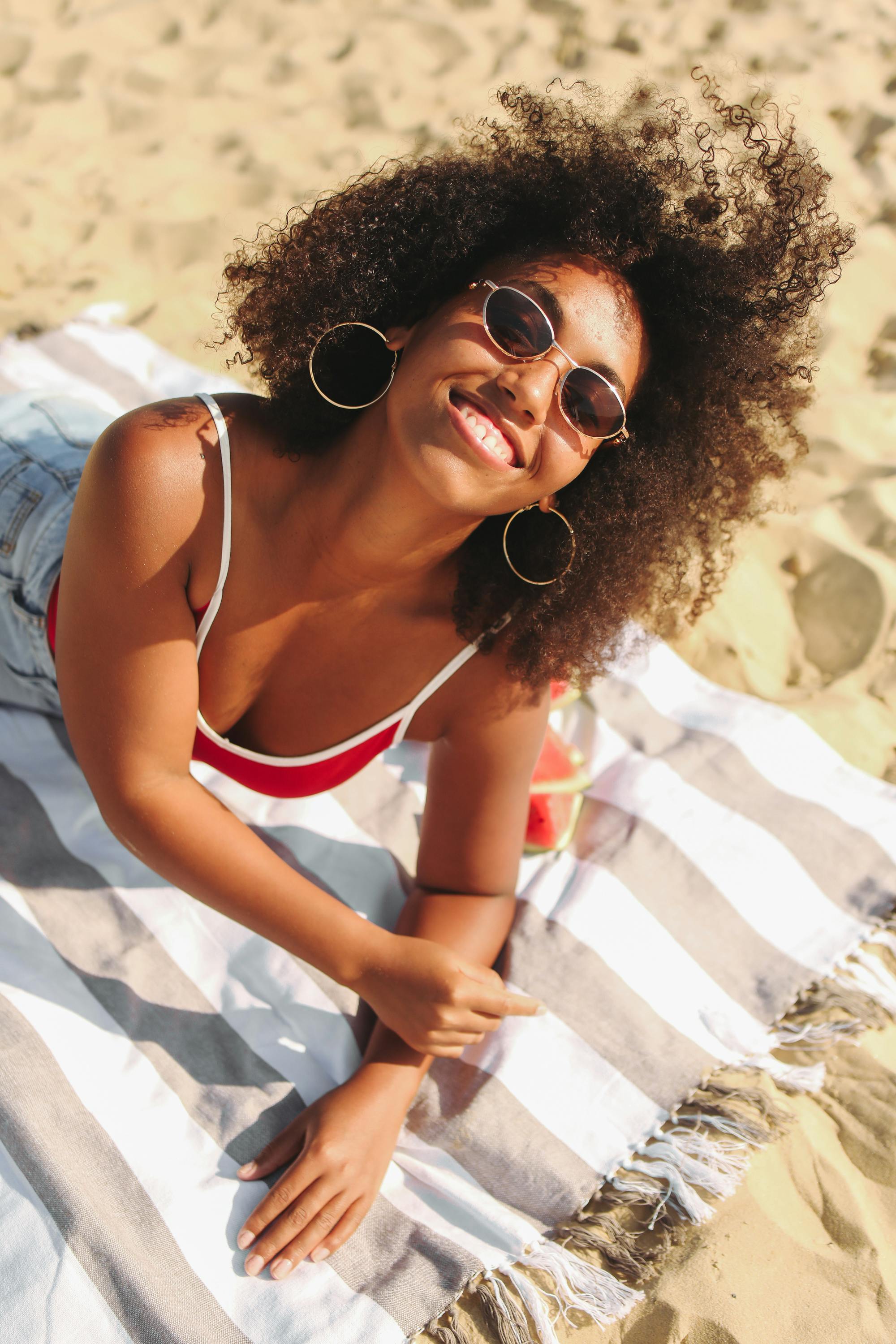 阳光明媚的海滩上，一位快乐的女人躺在条纹毛巾上，笑容灿烂