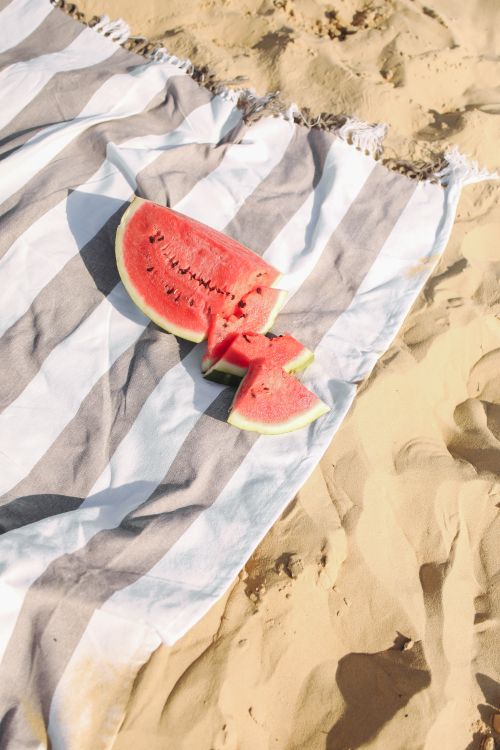 Free Fresh sliced watermelon on a striped beach towel over golden sand on a sunny summer day. Stock Photo