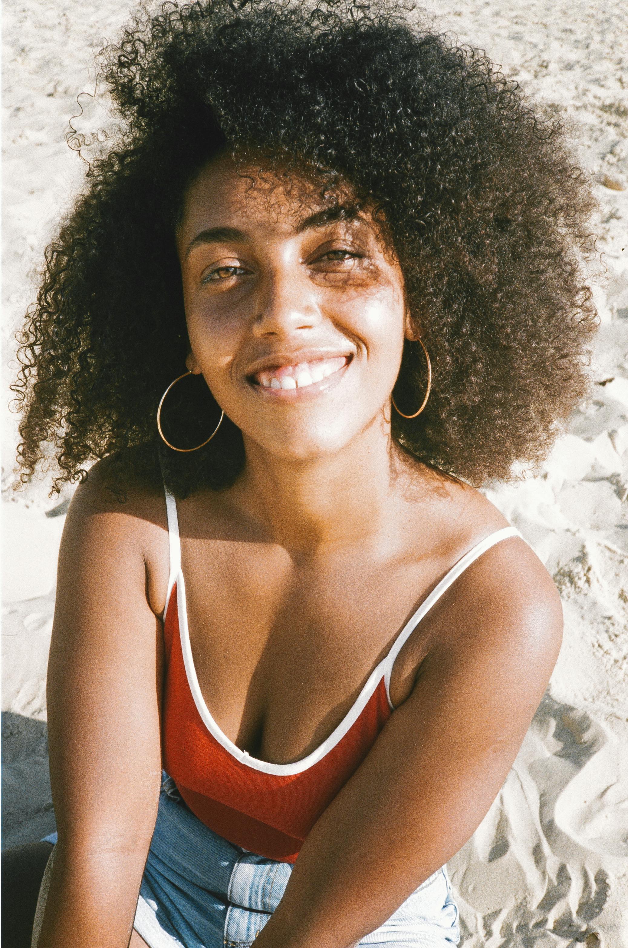 Portrait of a woman with afro hair and a smile, sitting on a sunny beach.