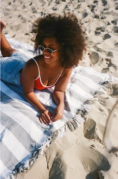 A woman in sunglasses and summer attire enjoying a sunny day on a beach blanket.