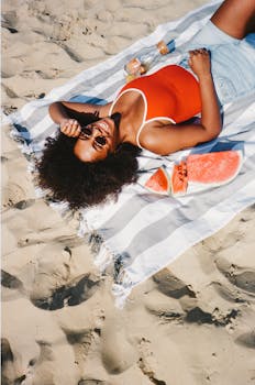 Smiling woman on a beach blanket enjoying watermelon in the sun.