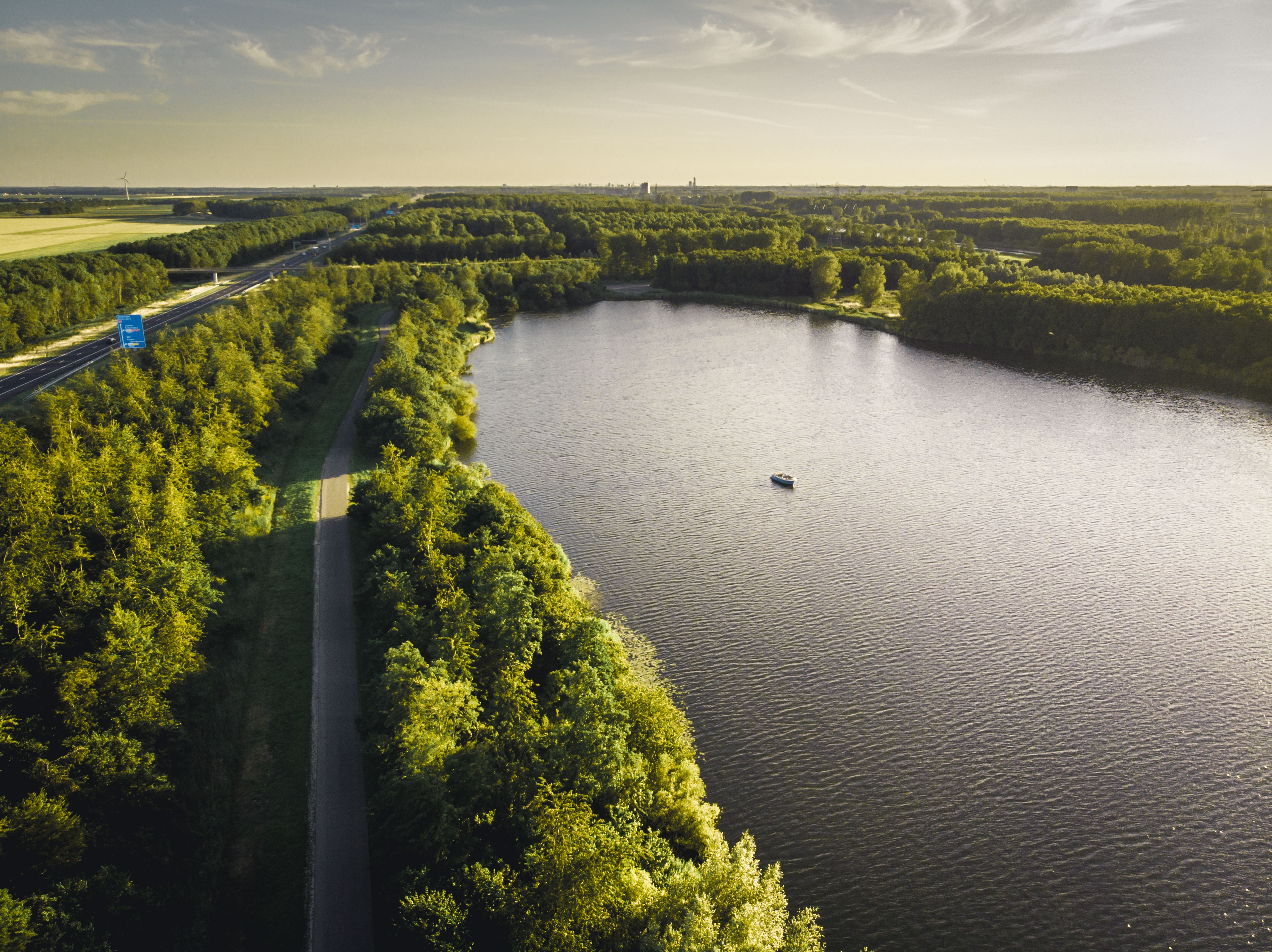 Spectacular drone view of boat floating on rippling lake surrounded by lush green endless woods and fields on sunny day