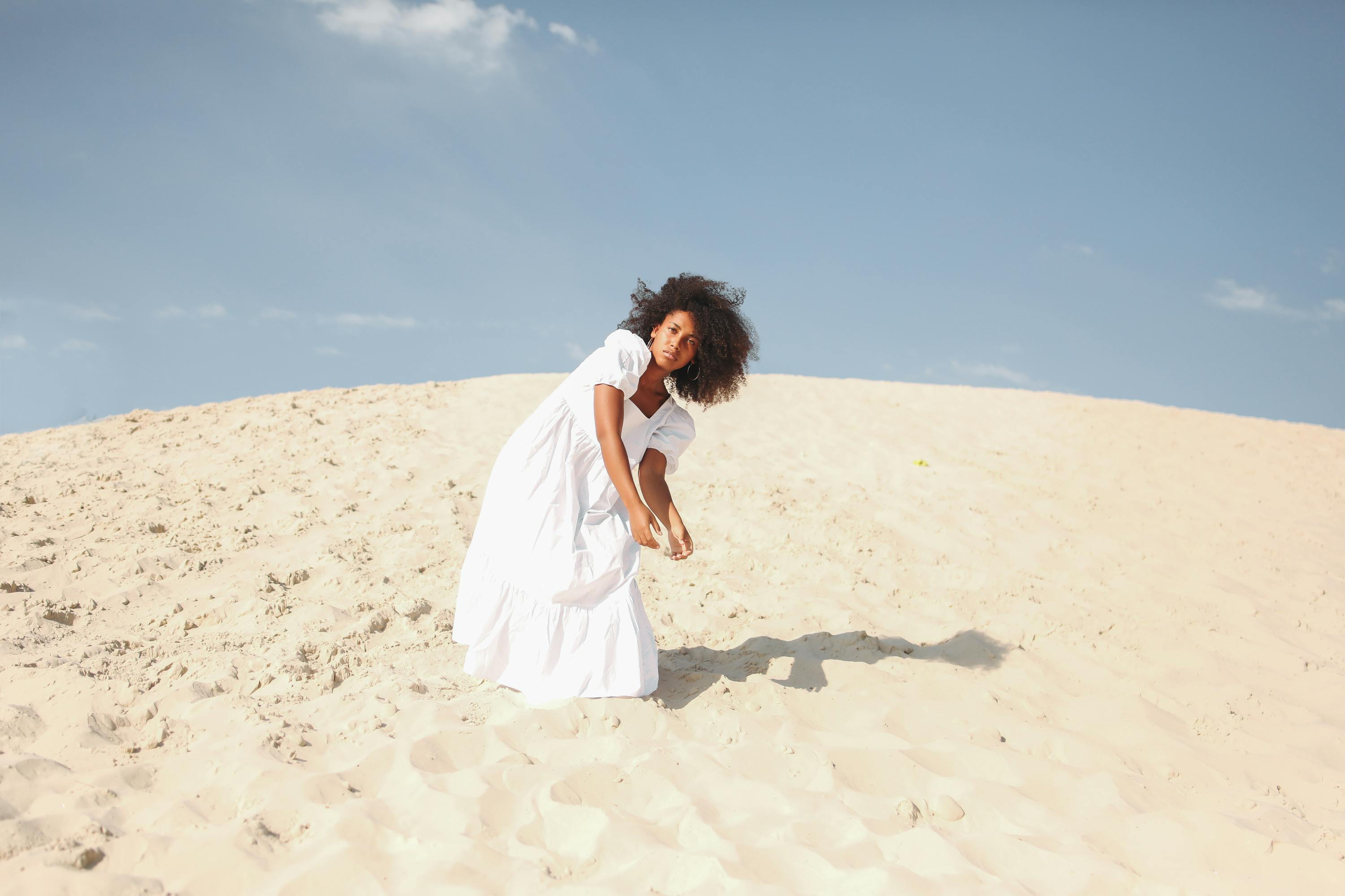 一名身穿白色连衣裙的女子，在阳光明媚的沙丘上摆出姿势，展现出自由与自然之美