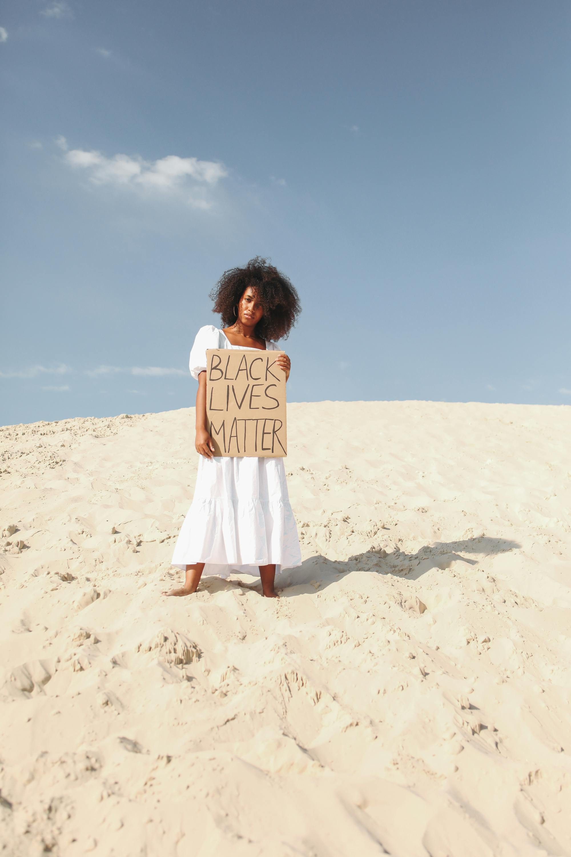 一名黑人妇女站在沙漠中，高举“黑人的命也是命”标语，强调自由与抗议