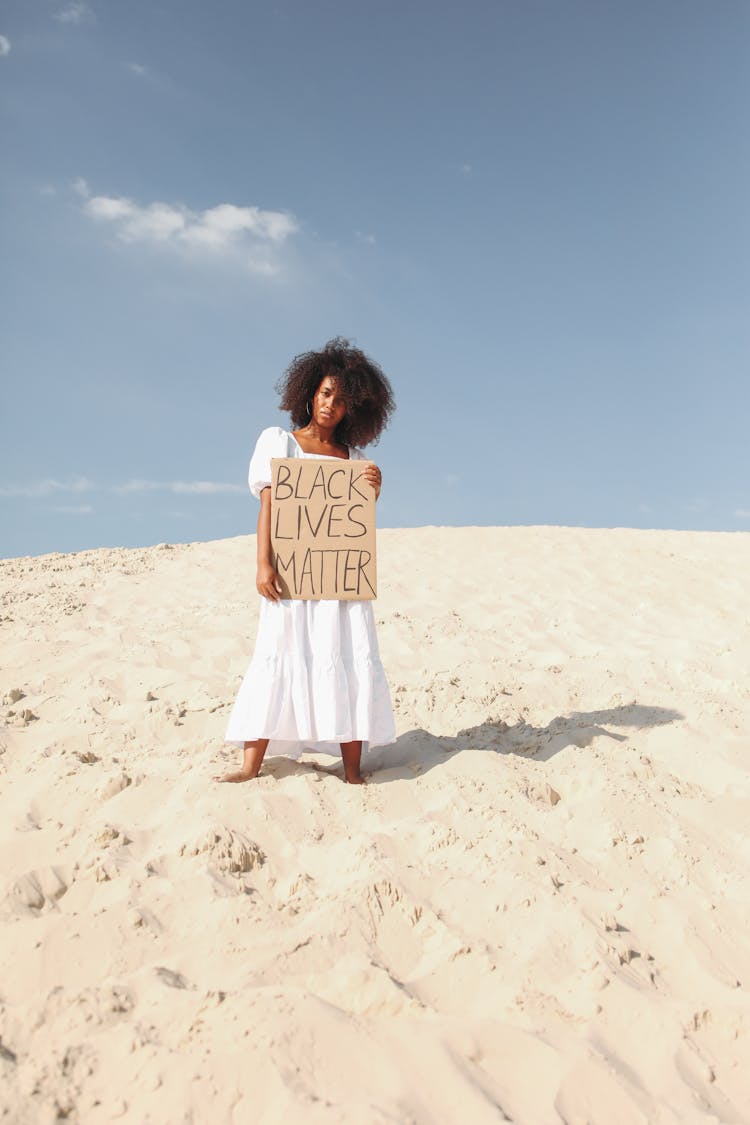 Woman Holding Poster In White Dress Standing On Sand