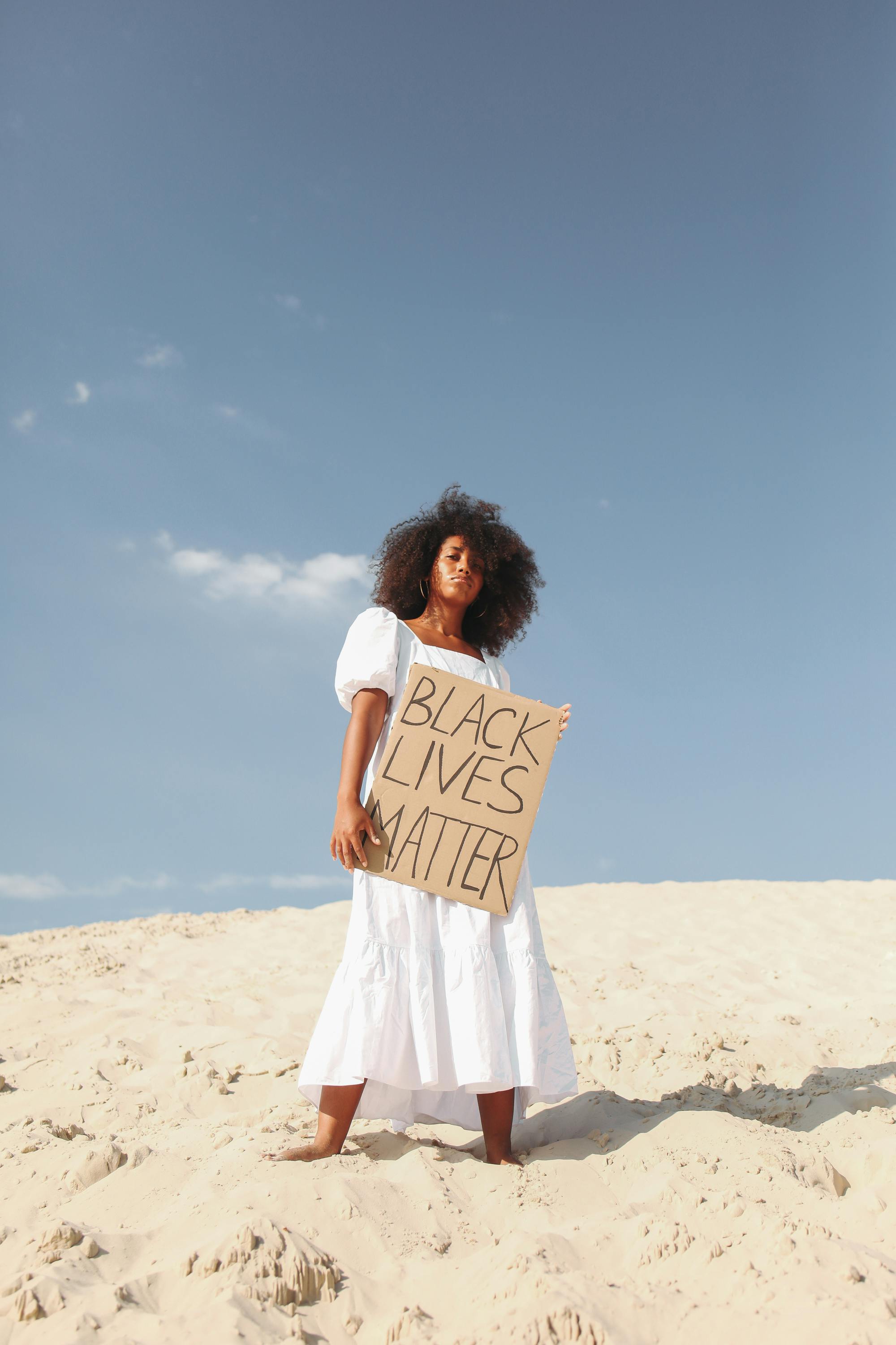 woman holding poster in white dress standing on sand