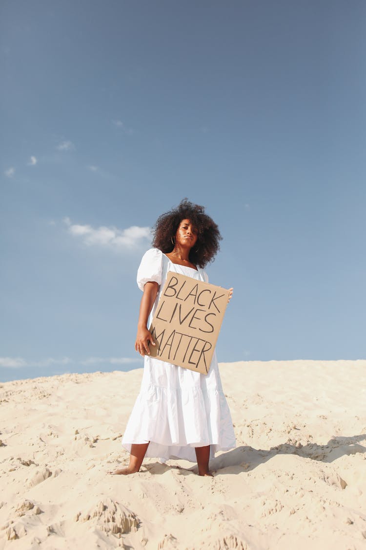 Woman Holding Poster In White Dress Standing On Sand