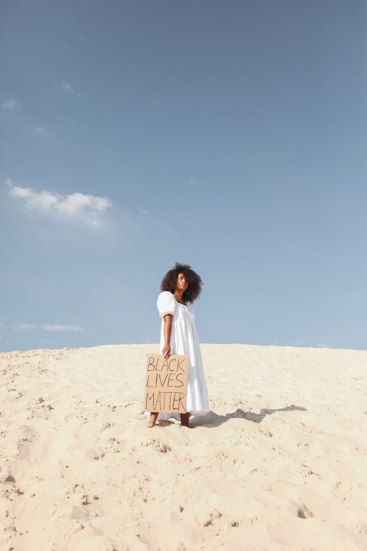 Woman Holding Poster In White Dress Standing On Sand