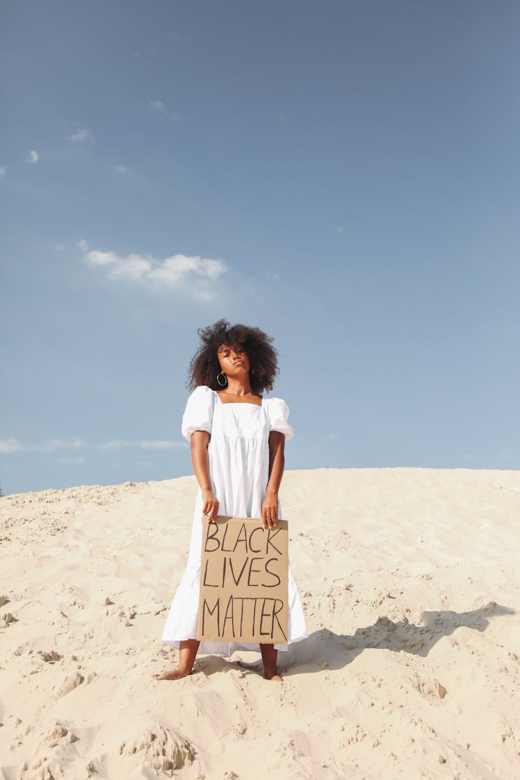 Woman Holding Poster In White Dress Standing On Sand