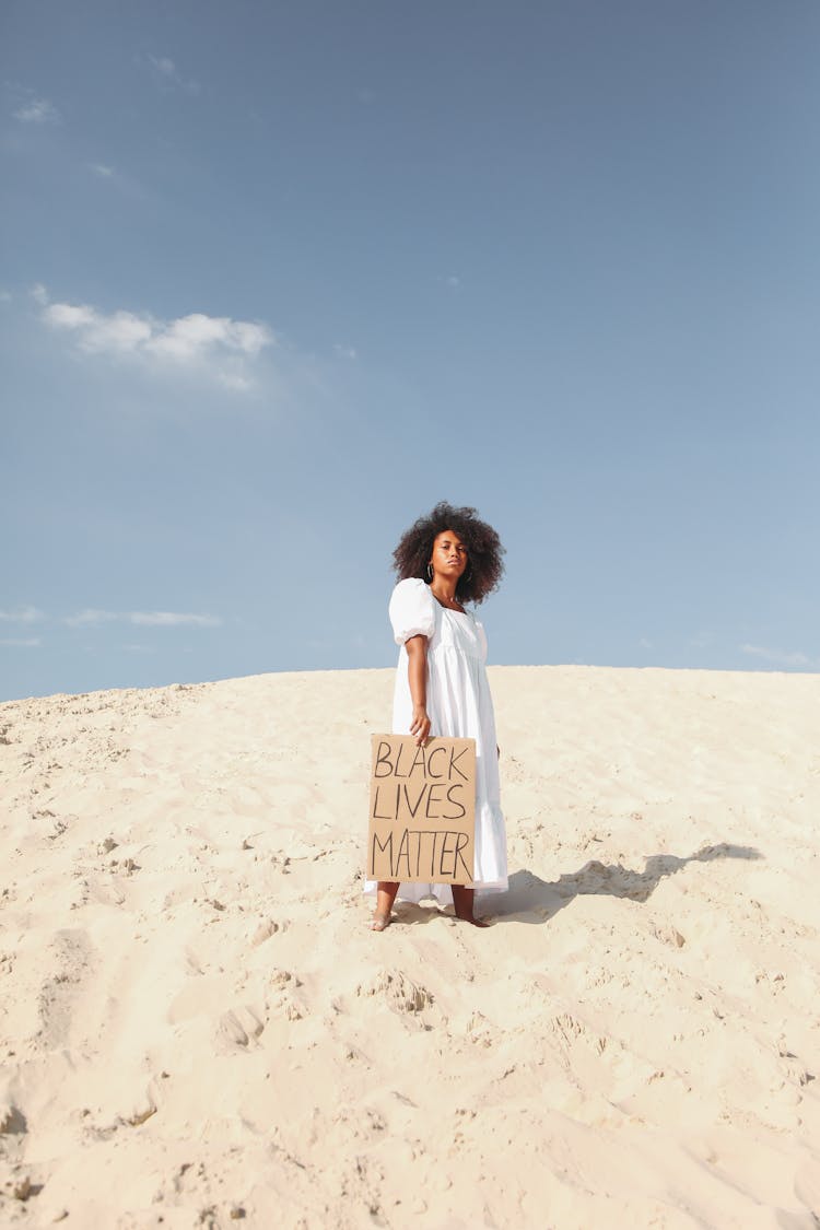 Woman Holding Poster In White Dress Standing On Sand