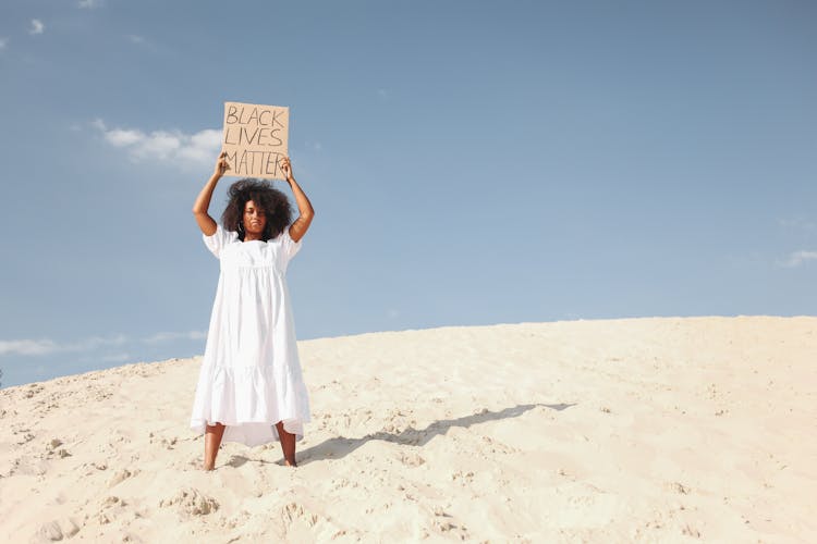 Woman Holding Poster In White Dress Standing On Sand