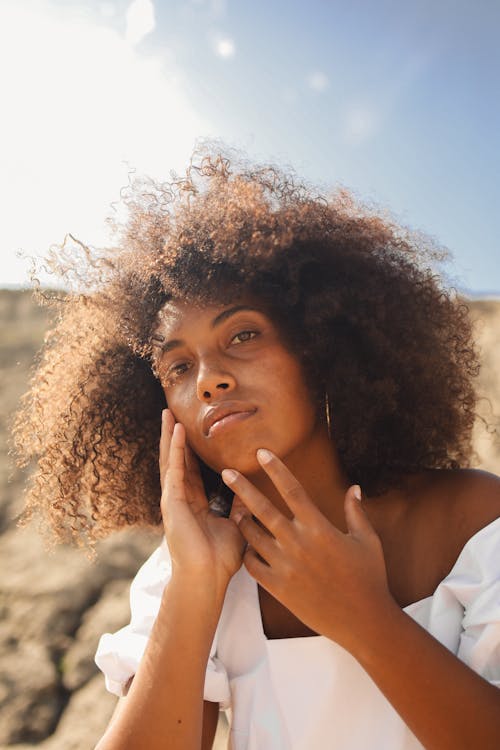 A Woman with Afro Hair Touching Her Chin while Looking at the Camera