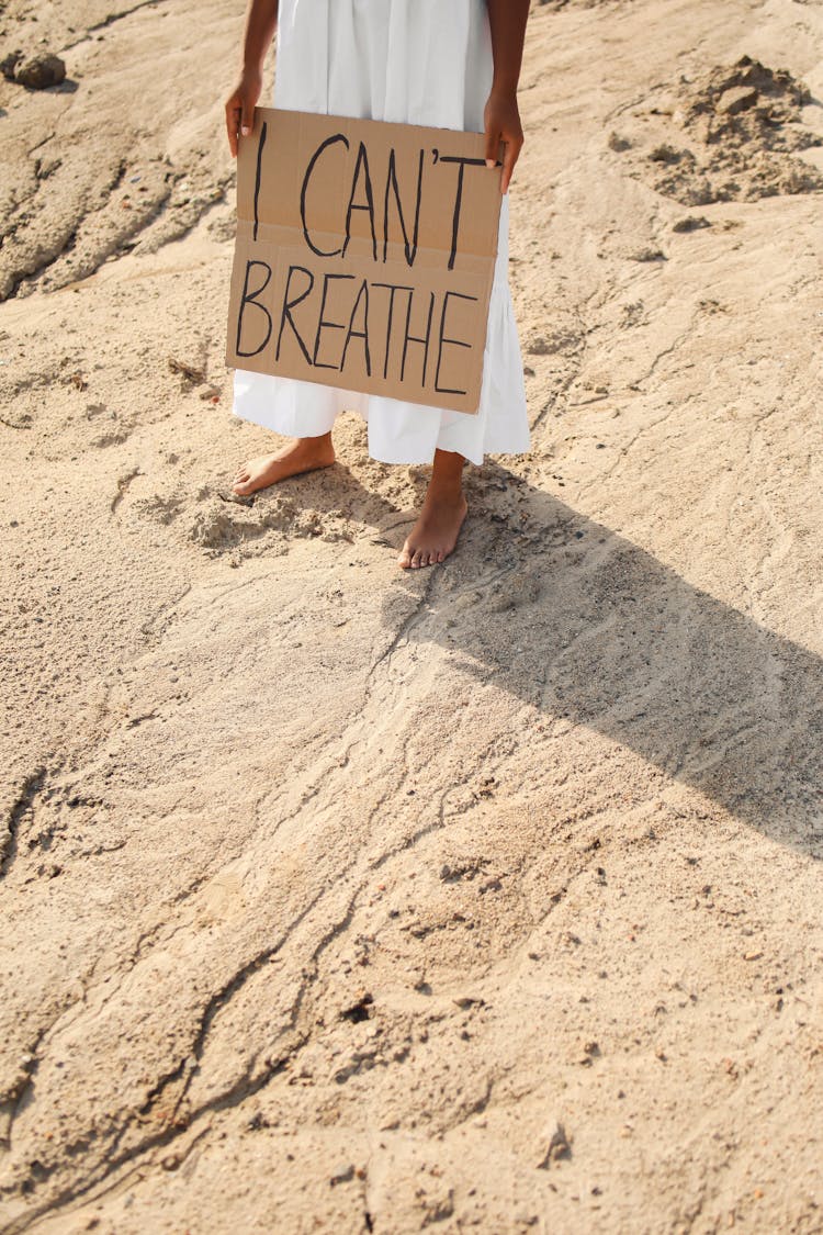 Person In White Dress Standing On Sand Holding A Poster